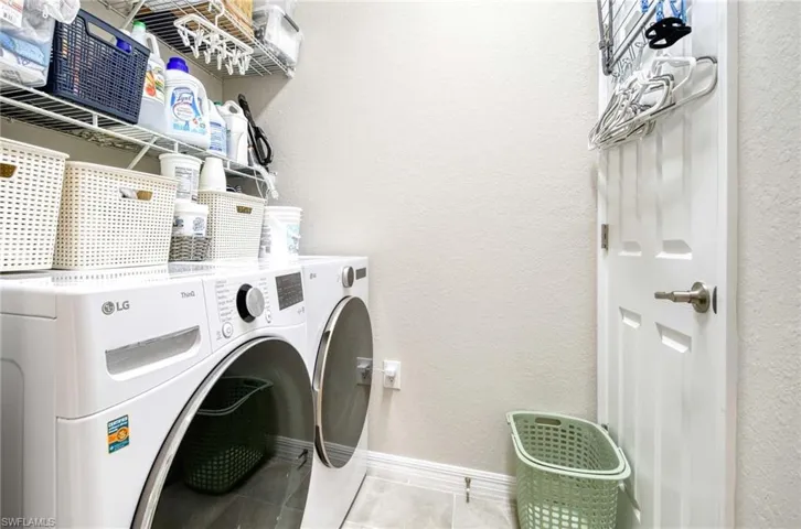 Laundry room featuring tile patterned flooring, washing machine and clothes dryer, and a textured wall