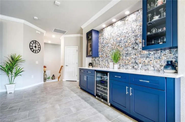 Indoor dry bar with glass insert cabinets, blue cabinetry, ornamental molding, wine cooler, and light stone countertops