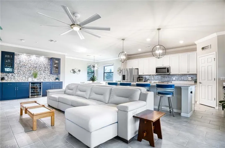 Living area with ornamental molding, bar, a chandelier, beverage cooler, and a ceiling fan