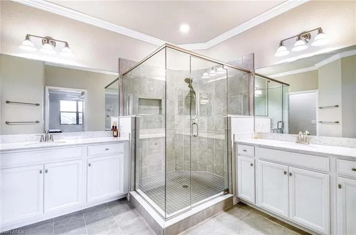 Full bathroom featuring ornamental molding, a stall shower, two vanities, and light tile patterned floors