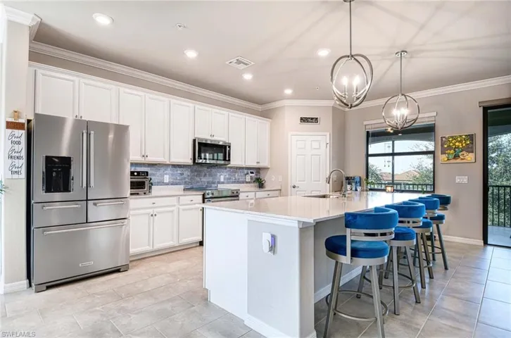Kitchen with stainless steel appliances, ornamental molding, a kitchen bar, a center island with sink, and white cabinets
