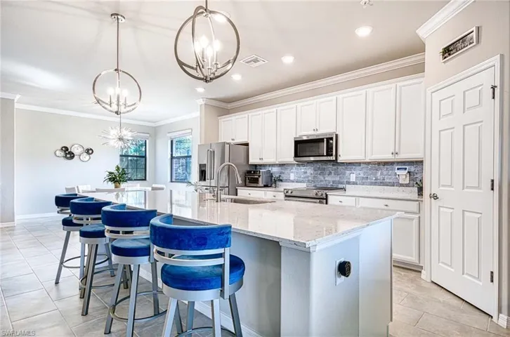 Kitchen featuring crown molding, a breakfast bar area, white cabinetry, hanging light fixtures, and a center island with sink