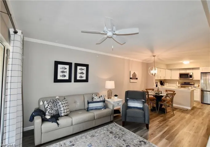 Living area featuring light wood-style floors, crown molding, a chandelier, and ceiling fan