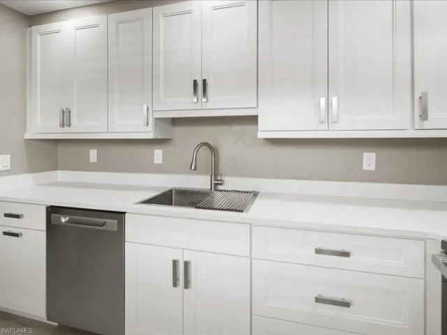 Kitchen with white cabinetry, stainless steel dishwasher, and light stone countertops