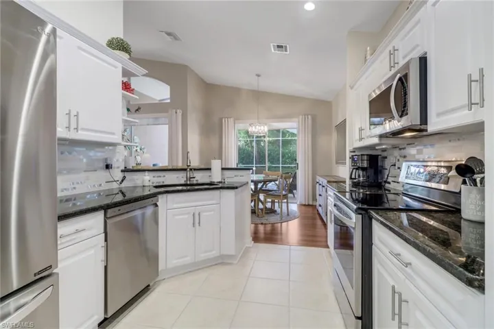 Kitchen featuring stainless steel appliances, lofted ceiling, white cabinets, open shelves, and decorative backsplash