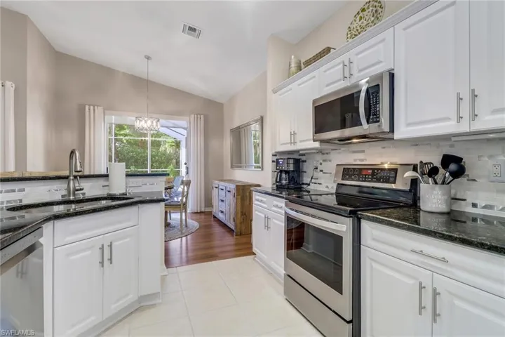Kitchen featuring appliances with stainless steel finishes, a chandelier, vaulted ceiling, decorative backsplash, and white cabinetry