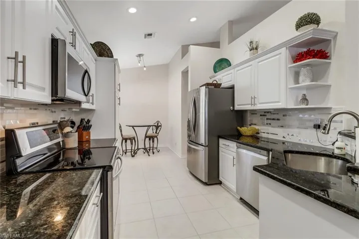 Kitchen featuring stainless steel appliances, decorative backsplash, white cabinets, dark stone counters, and light tile patterned flooring