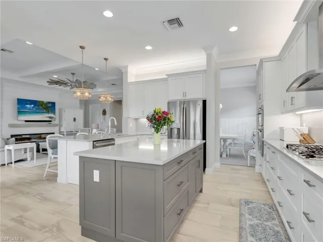 Kitchen with gray cabinets, hanging light fixtures, wall chimney range hood, open floor plan, and quartz counters