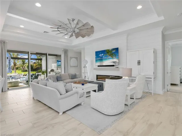 Living room with a glass covered fireplace, beamed ceiling, recessed lighting, wood walls, and a ceiling fan