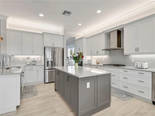 Kitchen featuring gray cabinetry, appliances with stainless steel finishes, quartz counters, a center island, and wall chimney exhaust hood