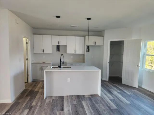 Kitchen featuring hardwood / wood-style floors, a kitchen island with sink, sink, decorative light fixtures, and white cabinetry