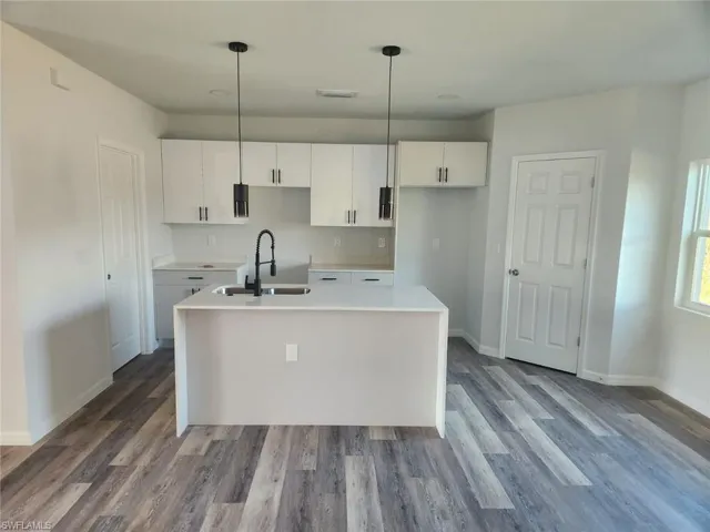 Kitchen with pendant lighting, sink, white cabinetry, and a kitchen island with sink
