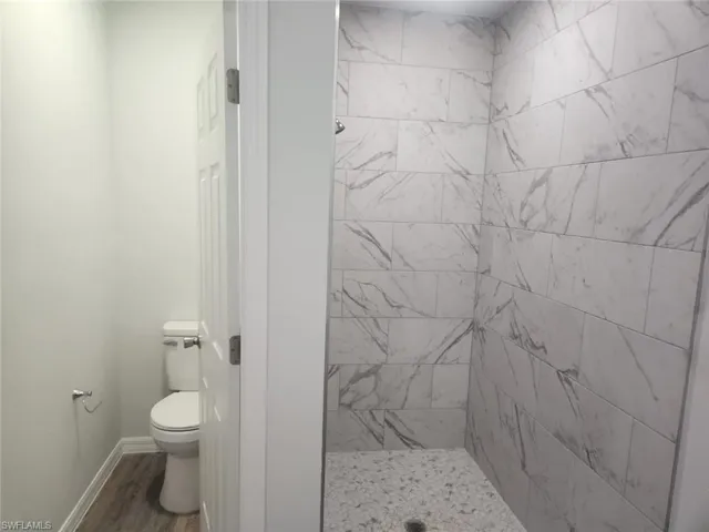Bathroom featuring a tile shower, hardwood / wood-style floors, and toilet