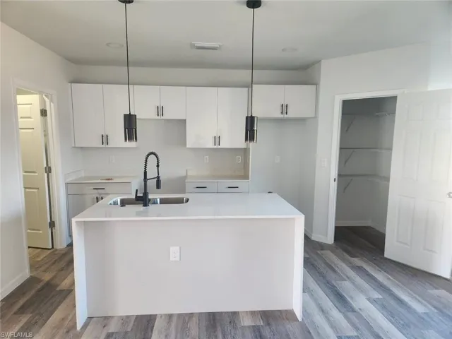 Kitchen featuring decorative light fixtures, sink, white cabinetry, and an island with sink