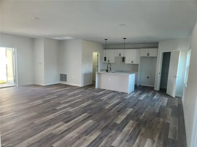 Kitchen with a kitchen island with sink, dark wood-type flooring, sink, pendant lighting, and white cabinetry