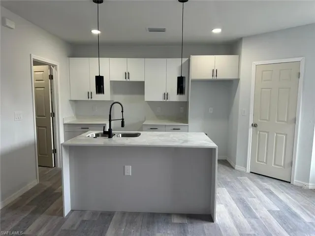 Kitchen featuring sink, white cabinets, pendant lighting, and a center island with sink