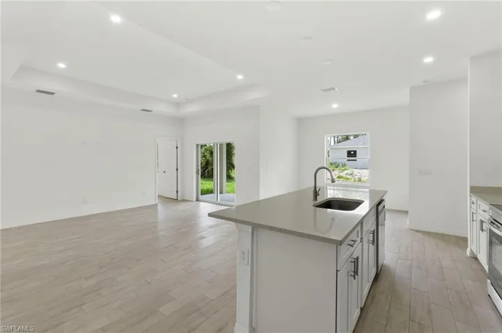 Kitchen featuring sink, an island with sink, light hardwood / wood-style flooring, and a raised ceiling
