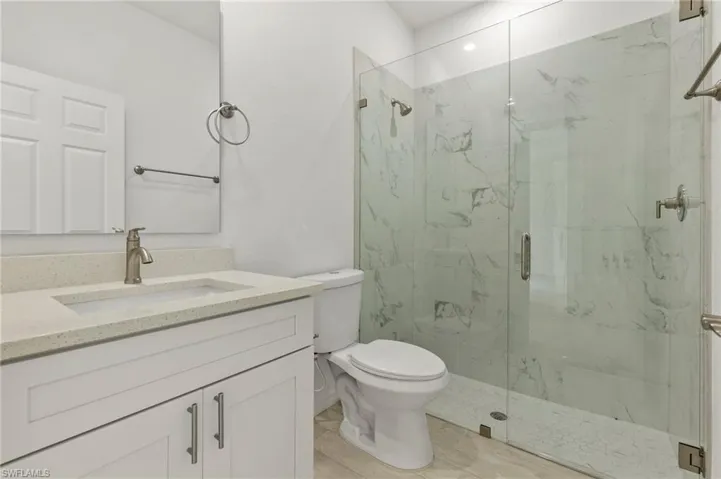 Bathroom with vanity with extensive cabinet space, toilet, and a shower with door