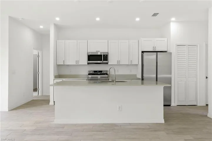 Kitchen featuring light hardwood / wood-style flooring, an island with sink, sink, white cabinetry, and appliances with stainless steel finishes