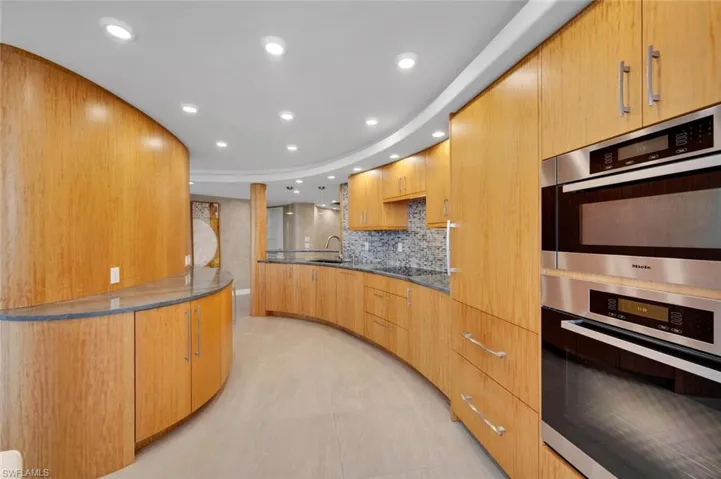 Kitchen featuring double oven, sink, backsplash, dark stone counters, and black electric cooktop