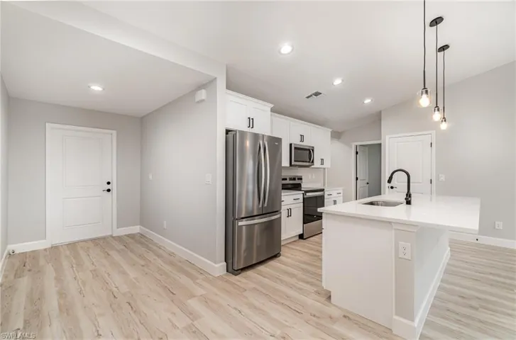 Kitchen featuring sink, appliances with stainless steel finishes, light wood-type flooring, and an island with sink