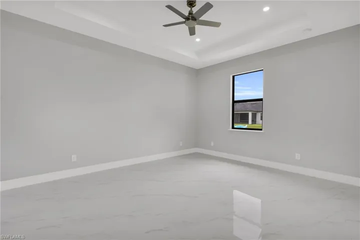 Empty room featuring a tray ceiling, recessed lighting, marble finish floors, and ceiling fan