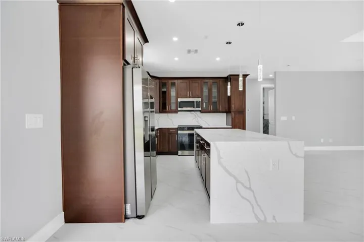 Kitchen featuring stainless steel appliances, a kitchen island, light marble finish floors, recessed lighting, and glass insert cabinets