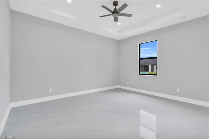 Empty room featuring a tray ceiling, recessed lighting, marble finish floors, and ceiling fan