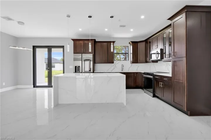 Kitchen with appliances with stainless steel finishes, a center island, light marble finish floors, recessed lighting, and dark brown cabinets