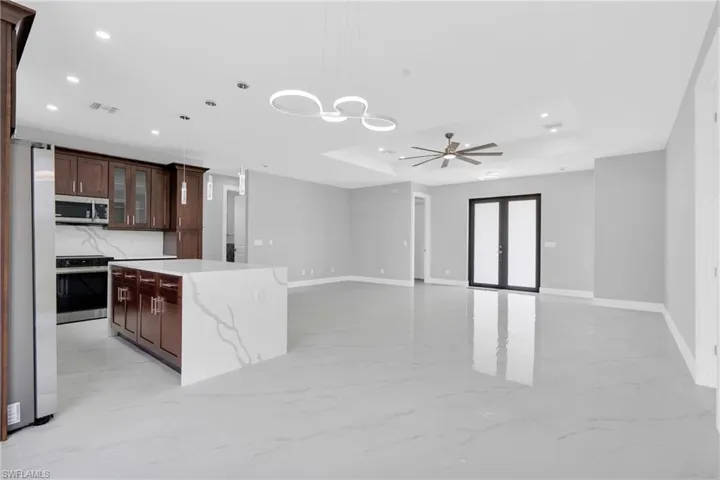 Kitchen featuring stainless steel appliances, recessed lighting, a raised ceiling, light marble finish flooring, and decorative light fixtures