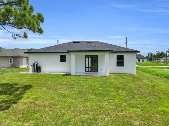 Back of house with a shingled roof, stucco siding, and a yard