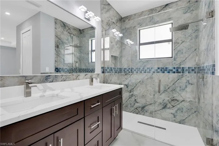 Full bath featuring tile walls, a marble finish shower, double vanity, and recessed lighting