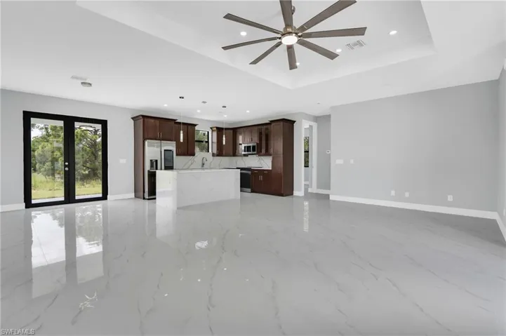 Unfurnished living room with ceiling fan, recessed lighting, light marble finish flooring, a raised ceiling, and french doors