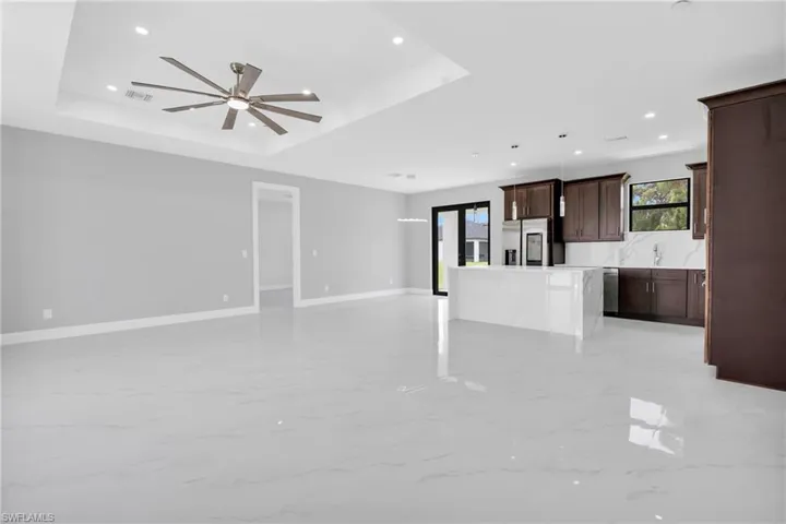 Unfurnished living room featuring a tray ceiling, ceiling fan, recessed lighting, and light marble finish flooring