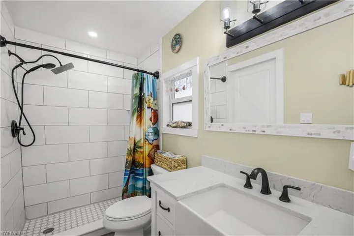 White subway tile shower enclosure with a mosaic tile floor, vanity with a rectangular undermount sink, and black-finish fixtures