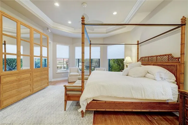 Bedroom with wood-type flooring, a tray ceiling, and crown molding
