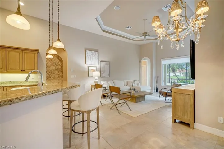 Kitchen featuring ceiling fan with notable chandelier, a breakfast bar area, light stone countertops, pendant lighting, and sink
