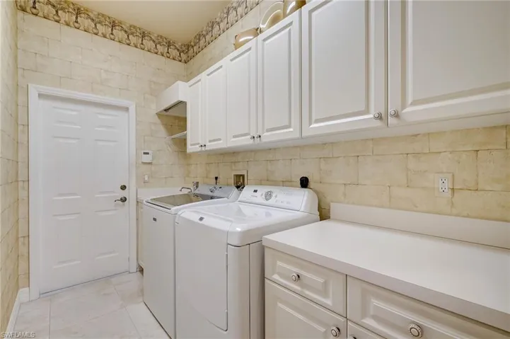 Clothes washing area with cabinets, light tile patterned floors, and washing machine and dryer