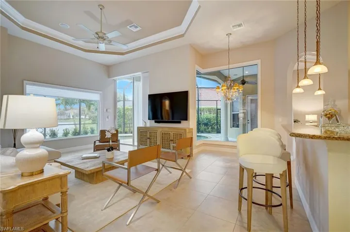 Tiled great room featuring ceiling fan with notable chandelier, ornamental molding, and a raised ceiling