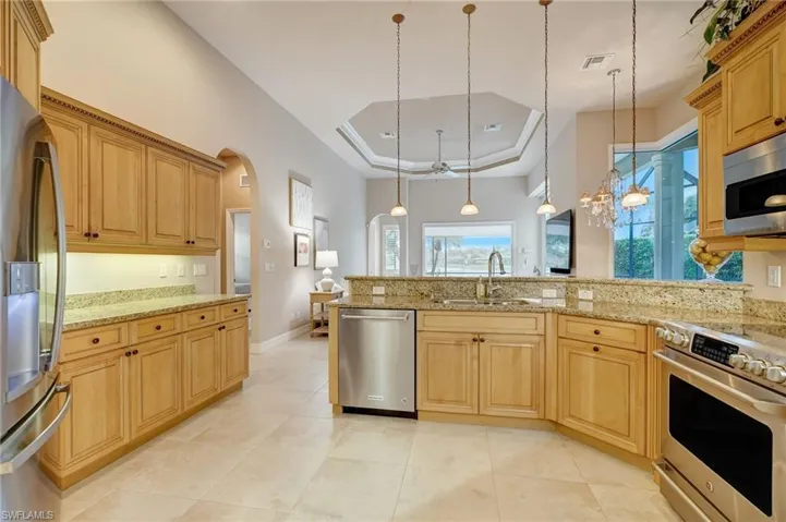 Kitchen featuring hanging light fixtures, sink, stainless steel appliances, a tray ceiling, and an inviting chandelier