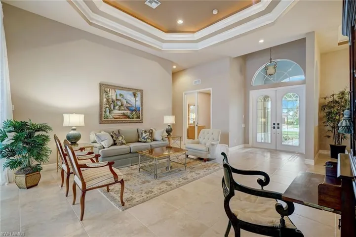 Tiled living room featuring a raised ceiling, ornamental molding, a towering ceiling, and french doors