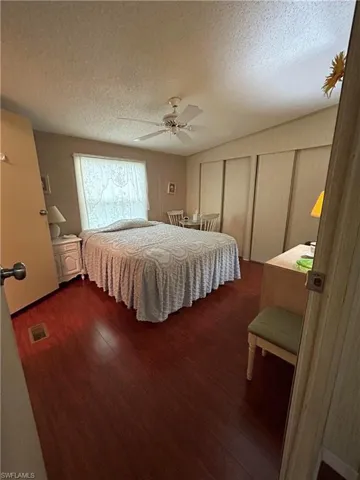 Bedroom featuring a textured ceiling, dark wood-type flooring, ceiling fan, and multiple closets
