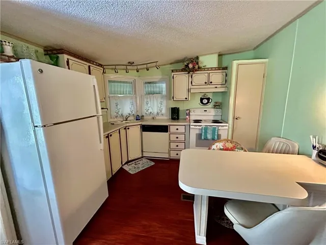 Kitchen featuring cream cabinetry, white appliances, a textured ceiling, a breakfast bar, and dark wood-type flooring