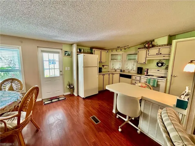 Kitchen with a textured ceiling, dark wood-type flooring, white appliances, and a kitchen bar