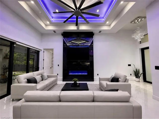 Recessed lighting, tray ceiling with accent lighting, and a prominent ceiling fan illuminate this living space