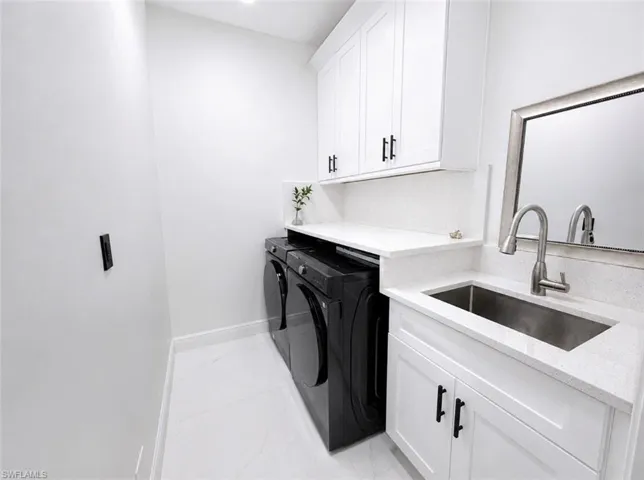 Laundry area featuring white cabinetry with black hardware, white countertops, a stainless steel sink with a gooseneck faucet, and white tile flooring
