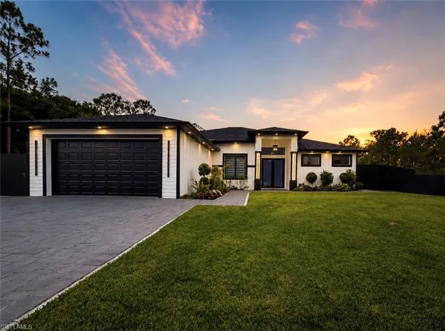 Contemporary single-story home featuring a black panel garage door, white vertical siding, and a black shingle roof