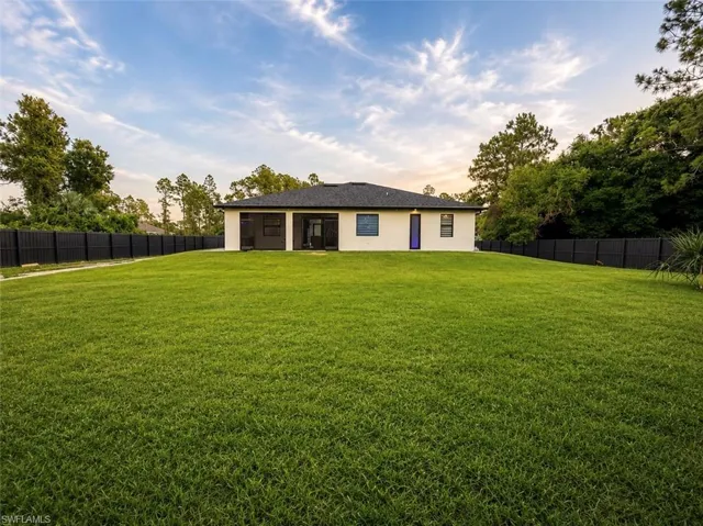 Expansive rear yard featuring a privacy fence, lush lawn, and mature trees
