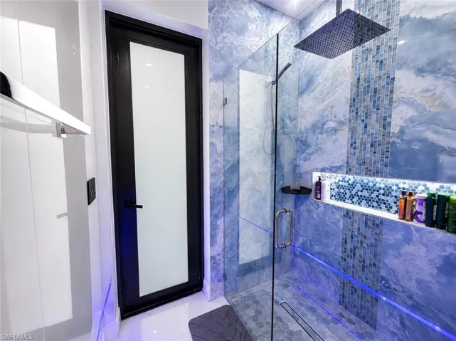 Shower featuring patterned blue wall tile, a rain shower head, glass enclosure, and an illuminated recessed niche