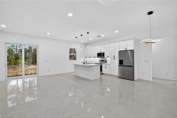 Kitchen featuring stainless steel appliances, white cabinetry, a kitchen island with sink, hanging light fixtures, and open floor plan